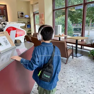 Black nylon kids chest bag with green Trend logo shown on a boy in a casual cafe setting