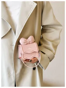Detail view of mini pink bow bag with metallic FAVE logo on khaki trench coat
