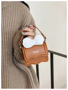Detail of brown mini handbag with white bow and FAVE text held by a model