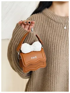 Brown mini handbag with white bow and wavy edge worn over a brown sweater