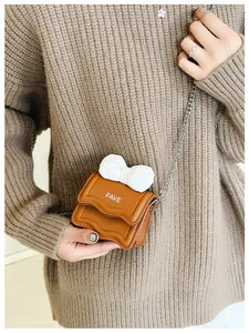 Detail of a brown mini crossbody bag featuring a white bow and silver chain strap