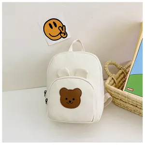 Detail of a beige canvas kids backpack with a cute brown bear patch and 3D ears design