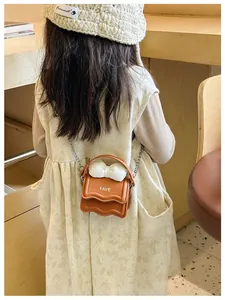 Detail of a brown mini crossbody bag for kids with a white bow and gold chain strap