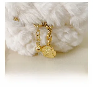 Detailed macro shot of white plush bag featuring golden zipper and camellia flower charm