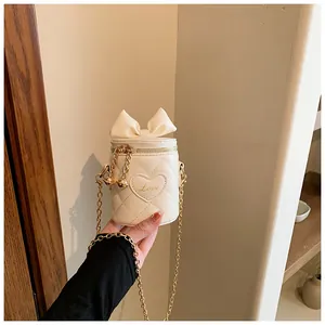 Detail of cream quilted bucket bag featuring a large bow and gold chain strap