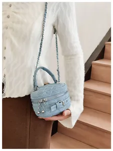 Close-up of quilted denim cylinder bag with silver metal buckle and woven chain strap