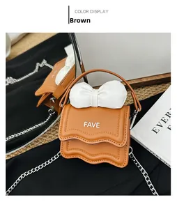 Detail of a brown crossbody mini bag with a white bow and silver chain strap