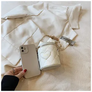 Close-up of white quilted mini bucket bag with gold chain and heart love embroidery