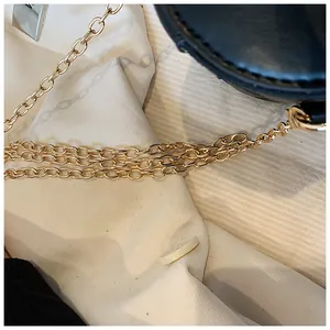 Detail of elegant gold woven chain strap connected to black leather bucket bag