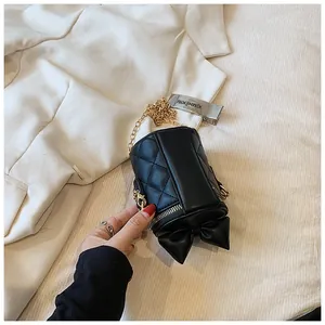 Detail of black quilted bucket bag with bow accent and gold chain on white fabric