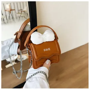 Detail view of mini caramel crossbody bag with white bow and silver chain link strap