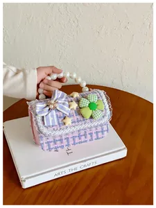 Detail van tweed kindertas met parelhandvat en kantafwerking op paarse geweven stof