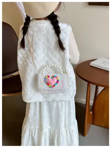 Dettaglio della borsa bimbi con grande cuore rosa, pompon colorati e manico di perle