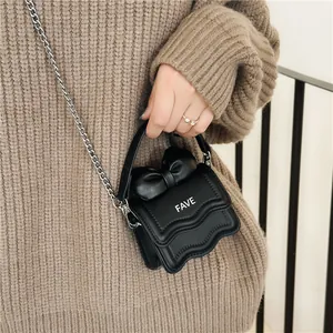 Black mini crossbody bag with wave flap and large bow handle worn with a brown sweater