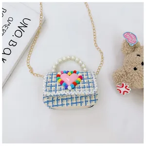 Dettaglio della borsa a tracolla in tweed con cuore rosa, pompon e manico di perle