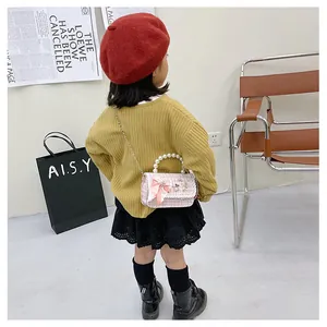 Detail of pink plaid kids crossbody bag with large bow and pearl handle on child model