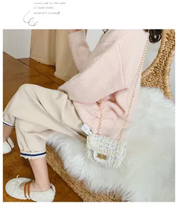 Detail of white tweed girl's bag with pearl decor, gold chain, and metal buckle
