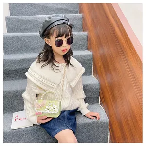 Detail of light green tweed kids bag with pearl handle and bow shown by child model