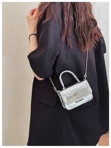 Detail of silver crocodile pattern mini crossbody bag with metal ball chain on a model