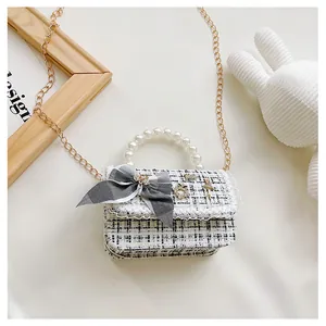 Detail of tweed crossbody bag featuring pearl handle and decorative bow with charms