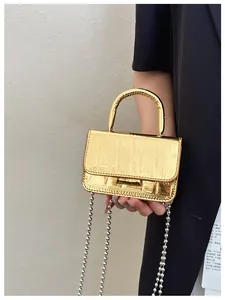 Detail of a golden metallic mini handbag with crocodile pattern and silver bead chain