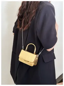 Detail of gold metallic mini bag with crocodile texture and silver chain strap on model