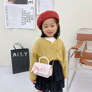 Pink tweed kids shoulder bag with pearl handle and bow, worn by child model
