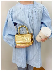 Detailed shot of a metallic gold mini PU handbag with crocodile texture and bead chain