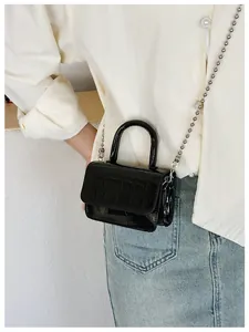 Detail of black mini crossbody bag with crocodile pattern and silver ball chain strap