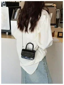 Detail of mini black patent leather trapezoid bag with silver metal bead chain strap