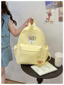 Detail of light yellow nylon kids backpack featuring fashion labels and a cute bear charm
