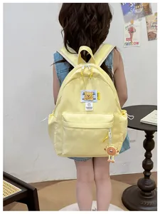Detail of yellow nylon children backpack with cartoon bear tag and adjustable straps