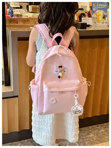 Pink kids backpack with star patch and cartoon pendant shown on a child in a cafe