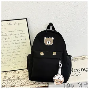 Detail of black nylon kids backpack featuring a cute bear patch and cupcake pendant