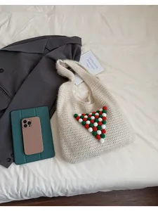 Detail view of beige knit tote bag featuring festive red green and white pom-pom accents