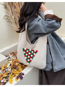 Detail of a white knit tote bag featuring festive red and green plush ball ornaments