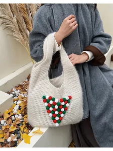 Detail view of winter knit tote bag featuring festive red and green plush pom-pom accents