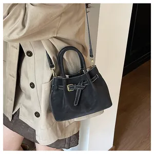 Détail d'un sac seau noir avec surpiqûres contrastées et boucles dorées sur modèle