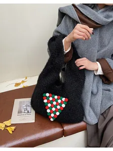 Close-up of black plush tote bag with festive red white and green pom-pom detail