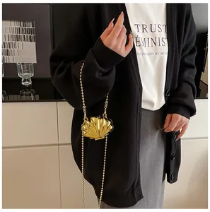 Detail view of the gold shell-shaped mini bag with a beaded metal chain on a model
