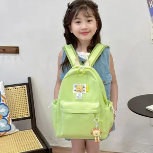 Green nylon kids backpack with cartoon charms shown on a young girl in a cozy home