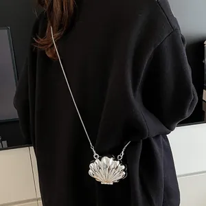 Silver shell-shaped mini crossbody bag with metallic finish and thin chain strap on a model