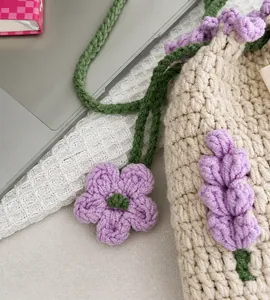 Detalle del bolso tipo cubo de ganchillo con flores púrpuras y cordón verde tejido