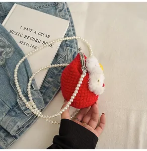 Close-up of red hand-knitted mini bag with white pearl strap and vintage metal clasp