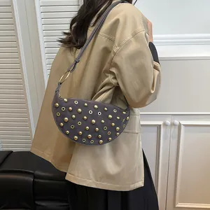 Detail of dark grey suede crescent bag featuring golden rivets and metallic eyelets