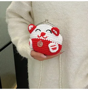 Detail of handmade knit lucky cat bag with red white yarn and gold blessing charm
