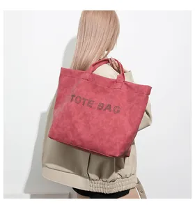 Detail of red leather tote bag showing riveted letters and textured surface on a model