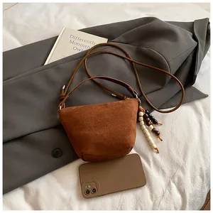 Nahaufnahme der braunen Wildleder-Mini-Beuteltasche mit Holzperlen-Anhänger auf Sakko