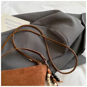 Detailansicht der braunen Wildlederstruktur und der Perlenquaste an der Handtasche