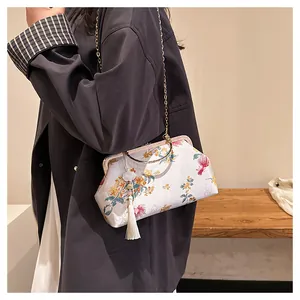 Detail of floral shell-shaped bag with metal ring handle and elegant white tassel charm